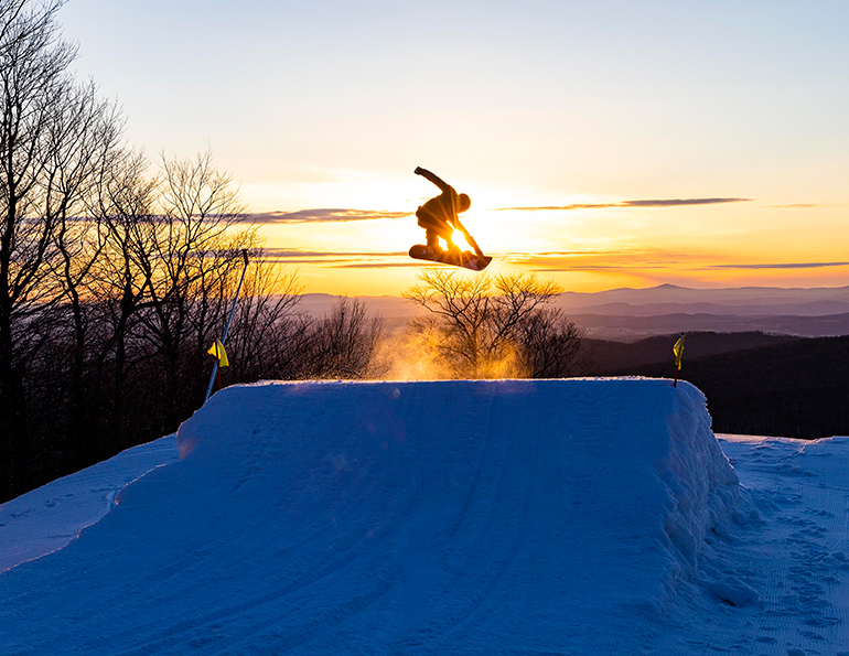 Athletic young girl jumping freely at mountain top against sunset